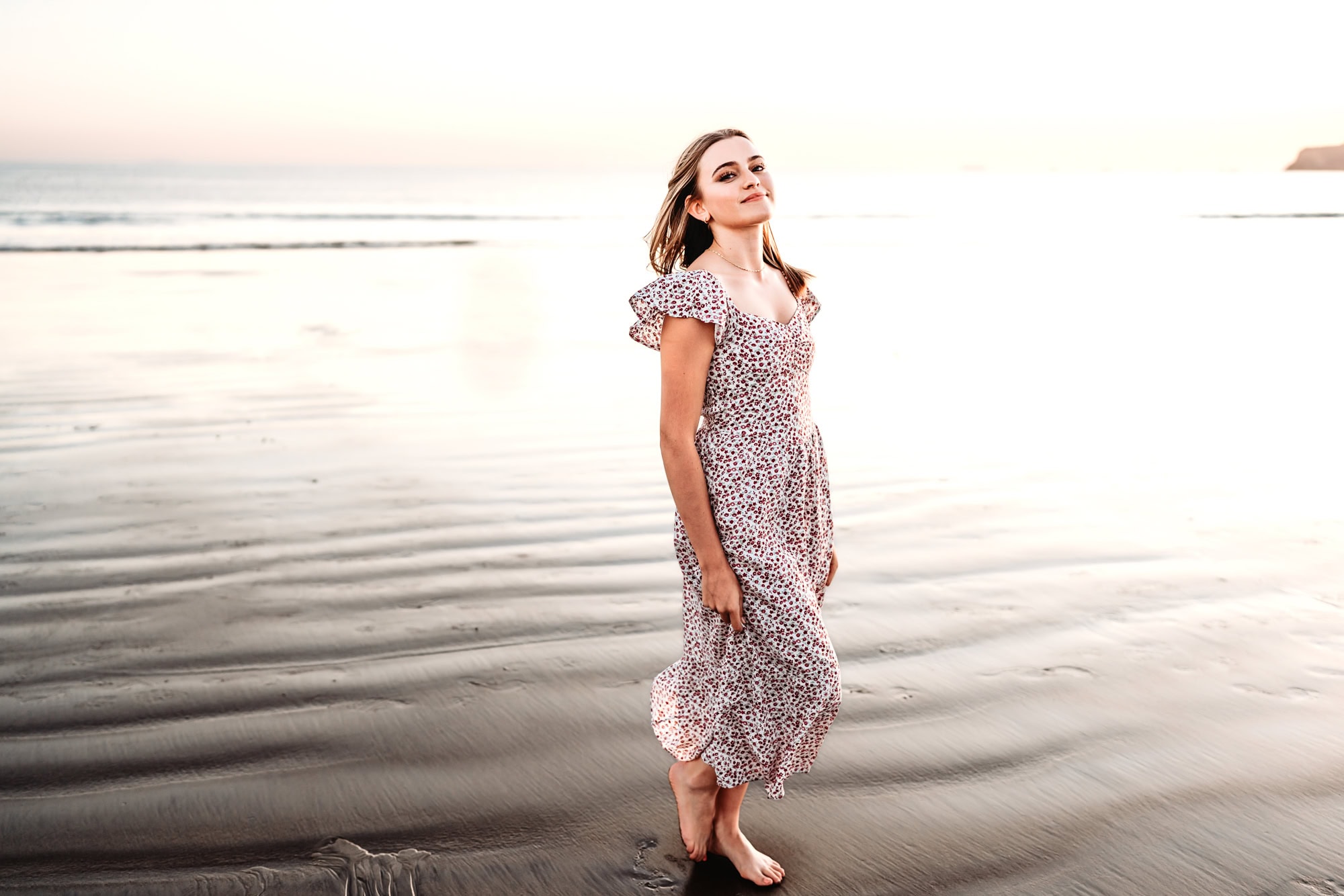 A young woman wearing dress stands on the shore during her photoshoot on Coronado Beach.