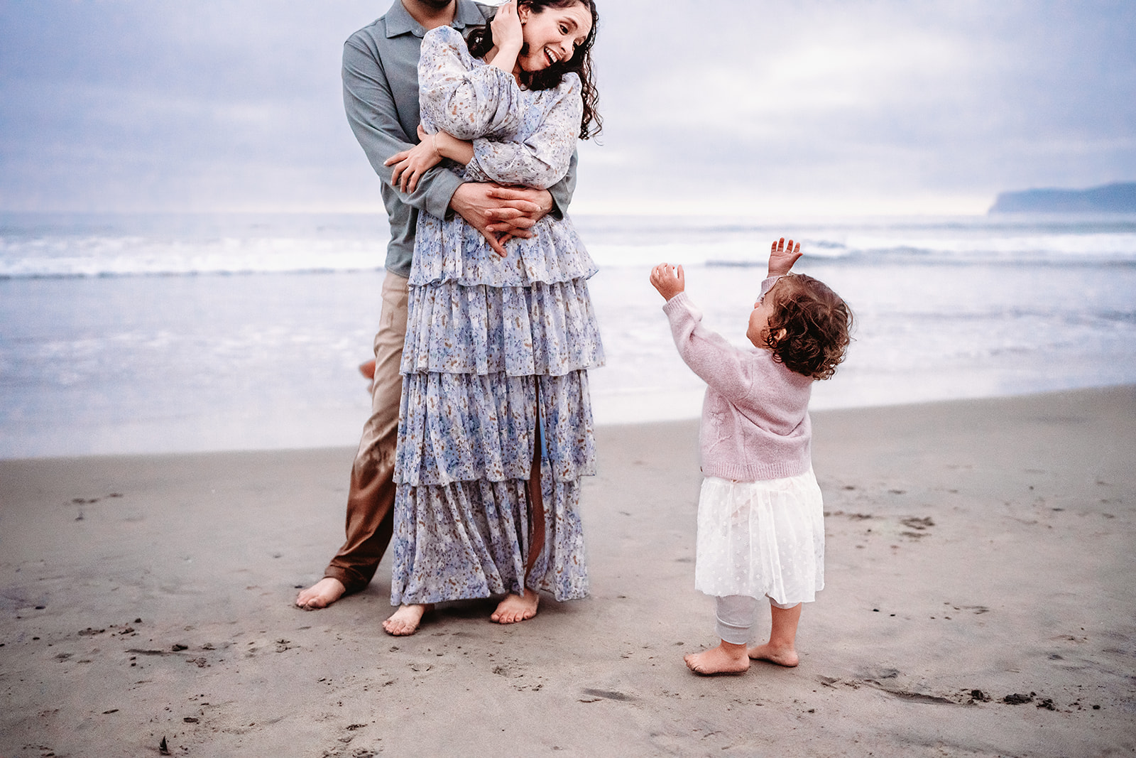 San Diego Family Photographer captures mother and father embracing while child looks on wanting to be held