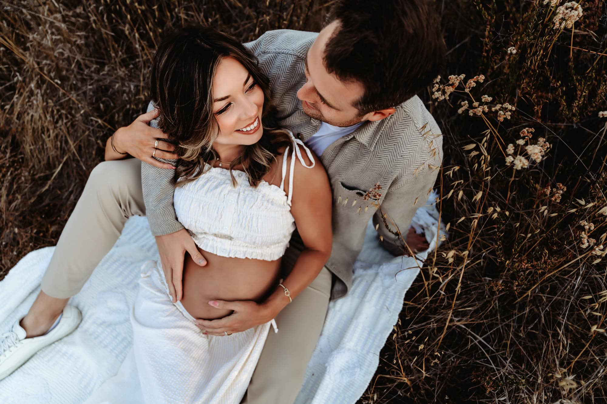 A pregnant woman snuggles up to her husband as they smile at each other during an outdoor maternity photoshoot in San Diego. 