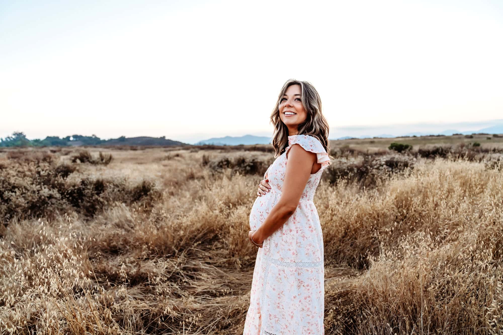 A pregnant woman holds her belly and smiles during a maternity photoshoot in San Diego. 