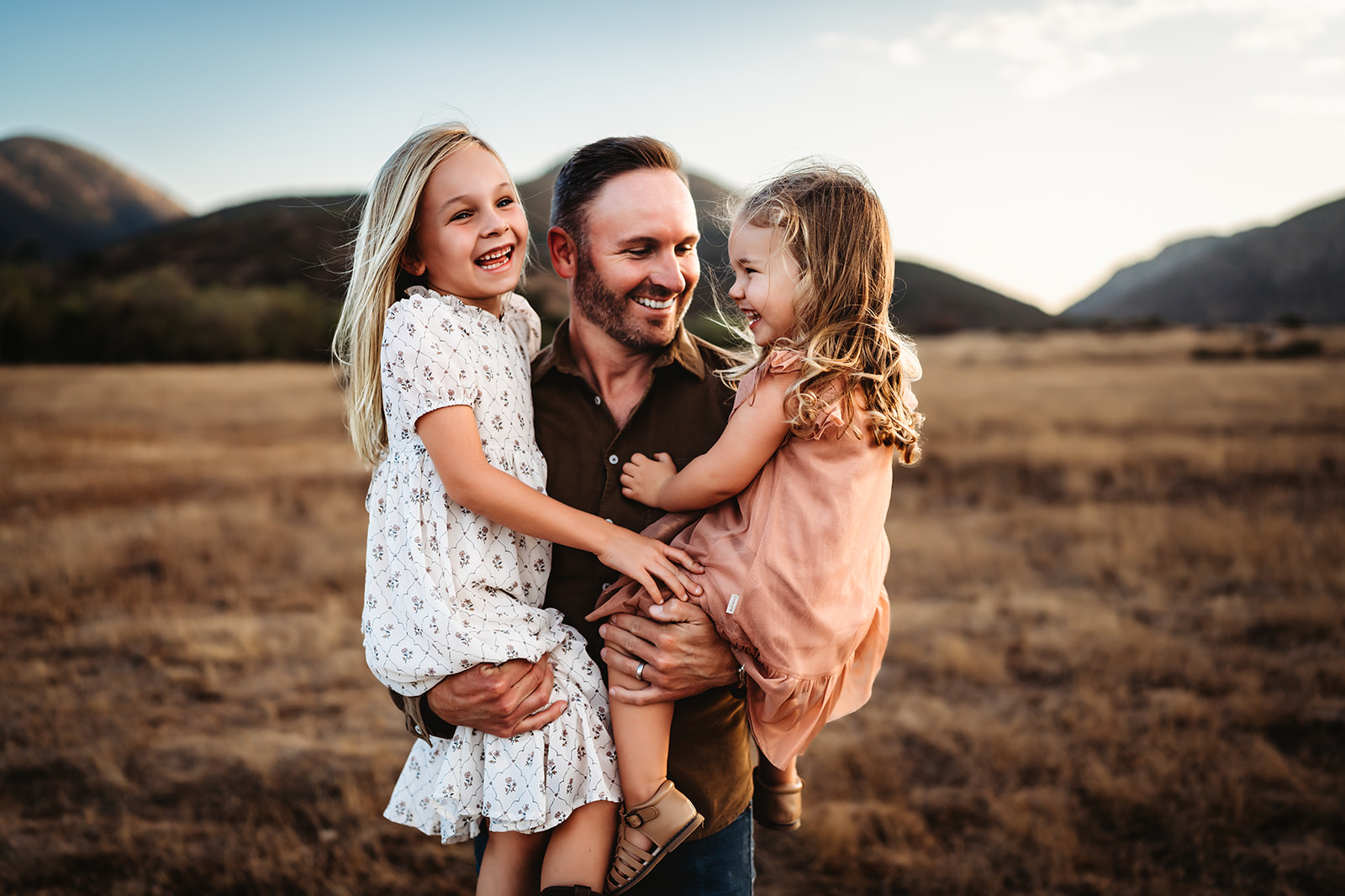 A man holds his two young daughters and makes them laugh during a Mission Trails family photoshoot in San Diego, CA.