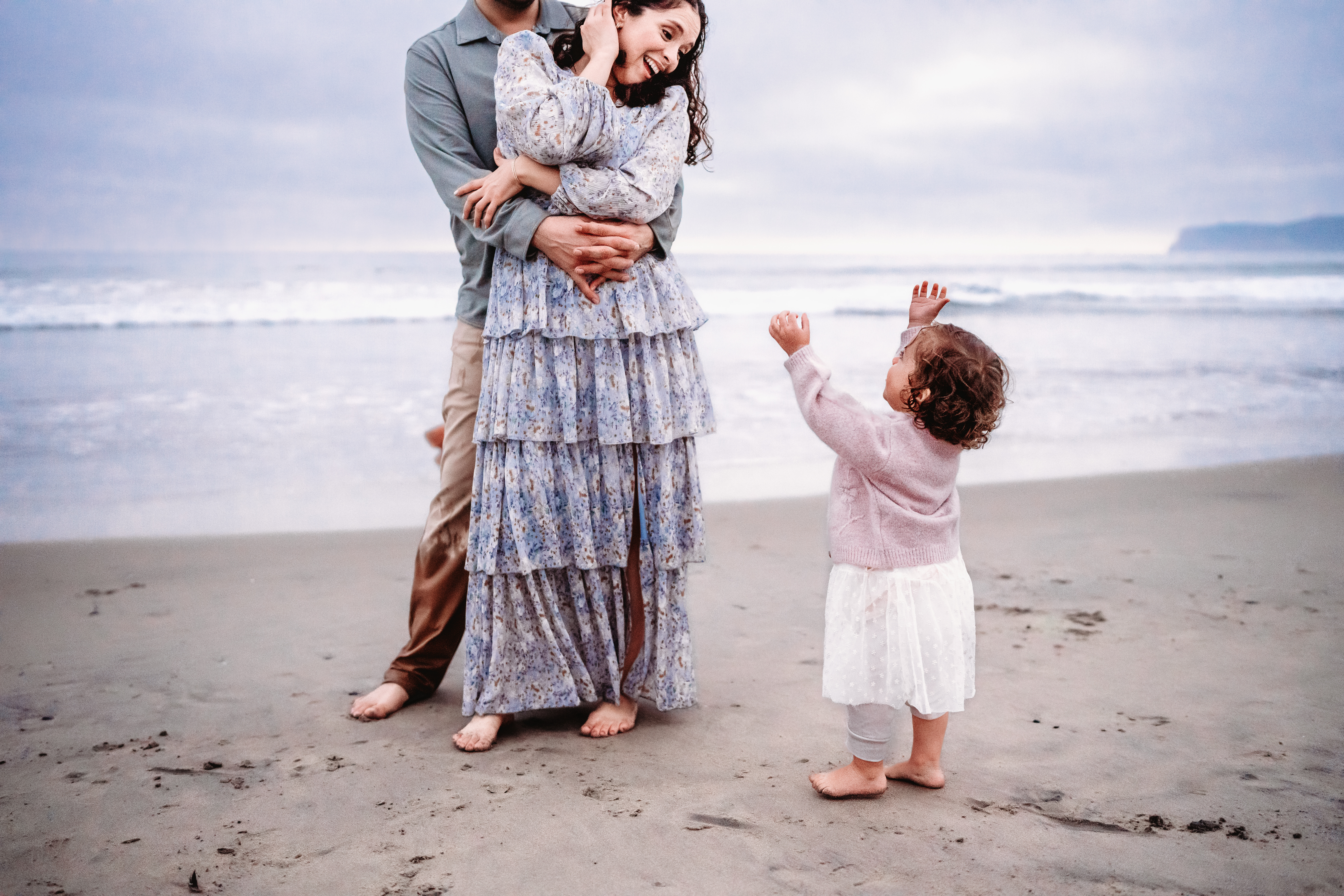 A toddler reaches for her mama on Coronado Beach during a sunset family photo session. 
