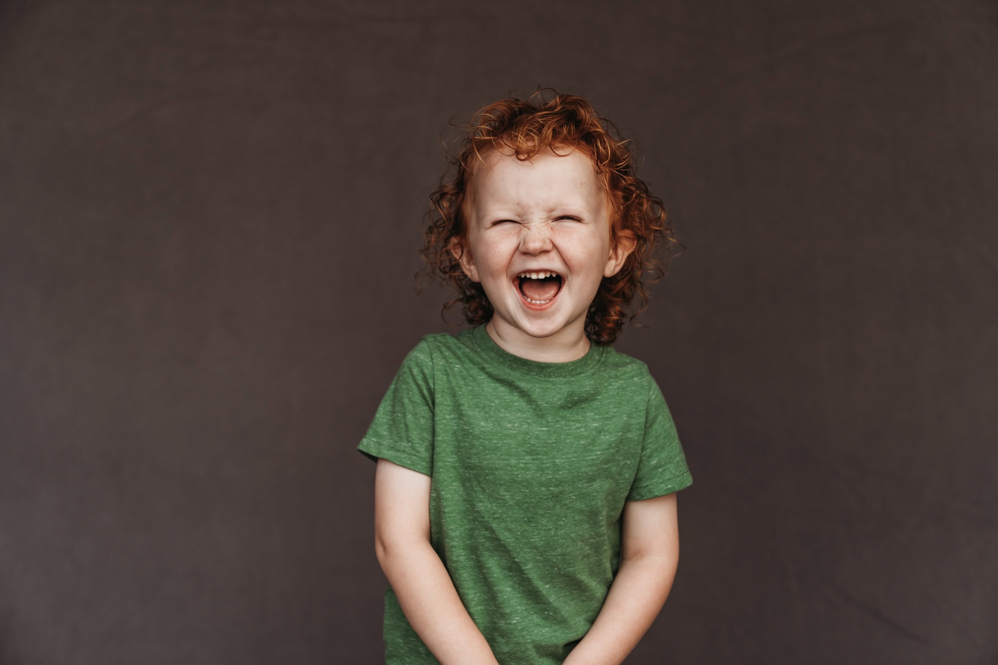 San Diego school photographer fine art homeschool portrait of young boy with curly red hair laughing joyfully in green shirt.
