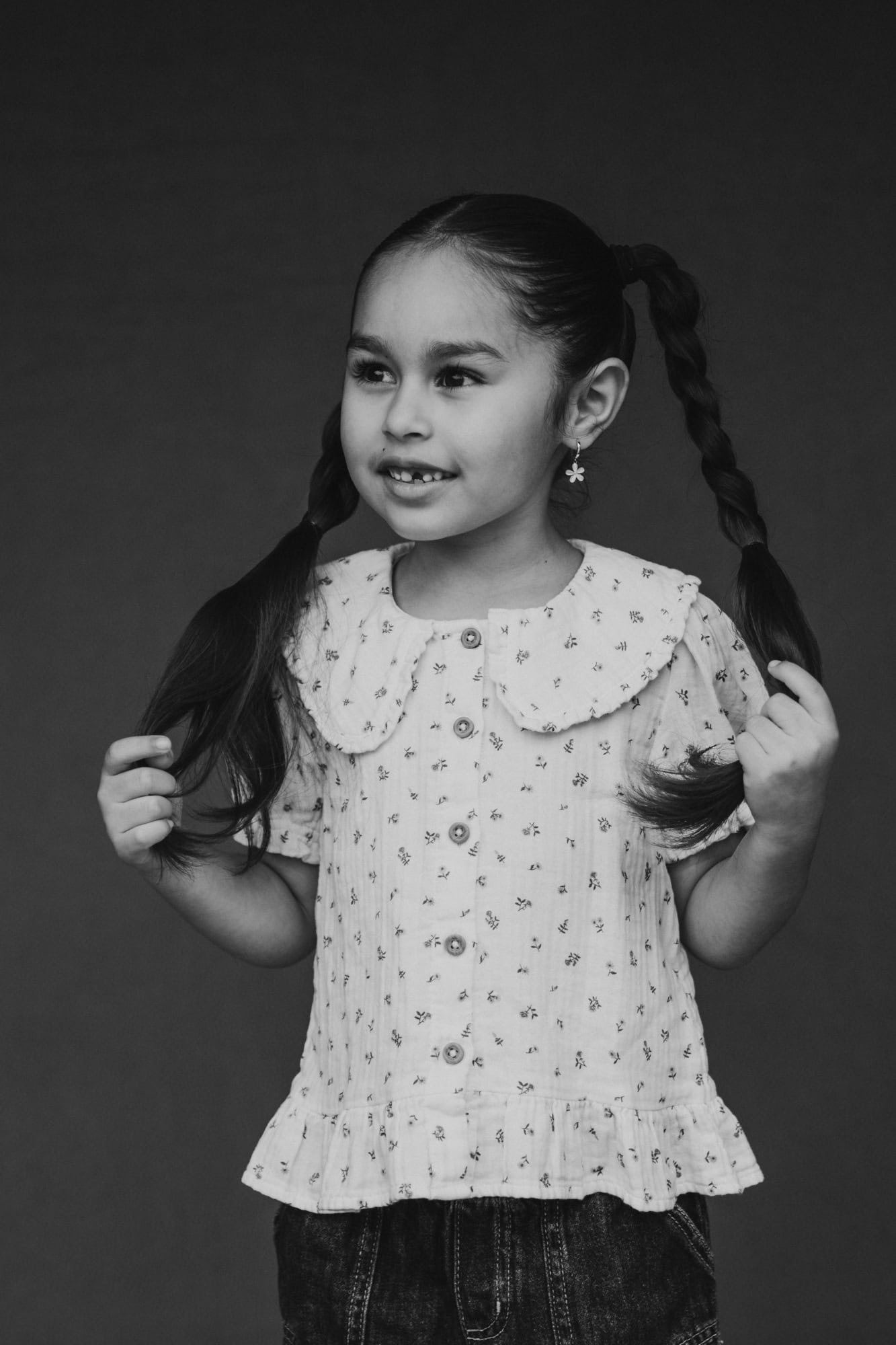 Fine art homeschool school photo by San Diego school photographer of young girl with pigtail braids, smiling softly and holding her hair.