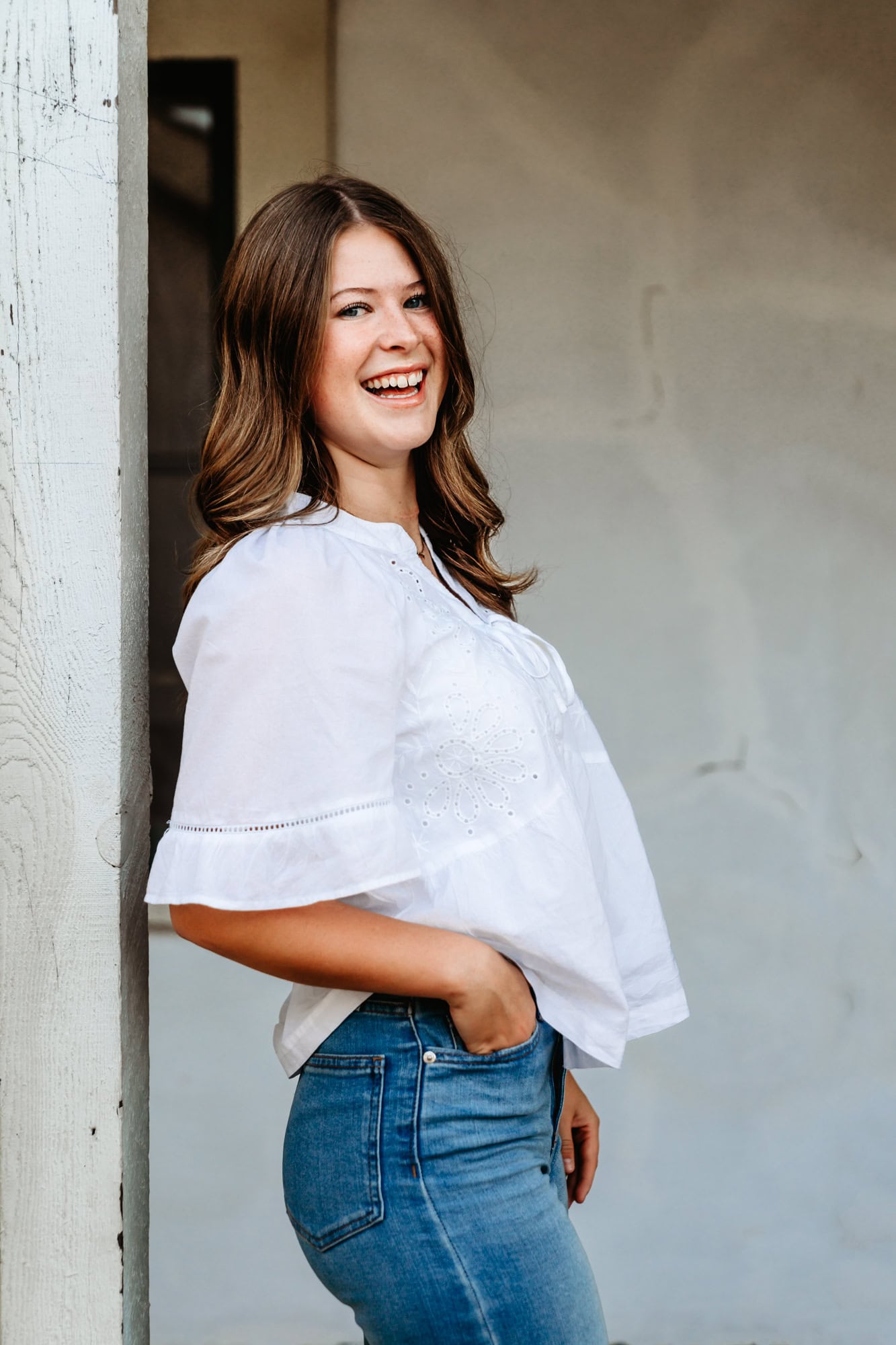 Senior girl leaning against a rustic white wall at the RP Ranch house, smiling in casual outfit during San Diego senior portraits