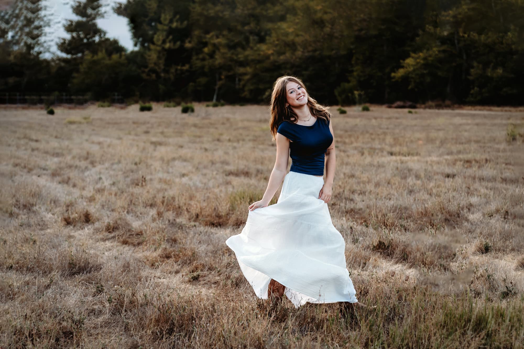 Senior girl twirling in an open grassy field wearing a long skirt, golden hour senior portraits in San Diego.