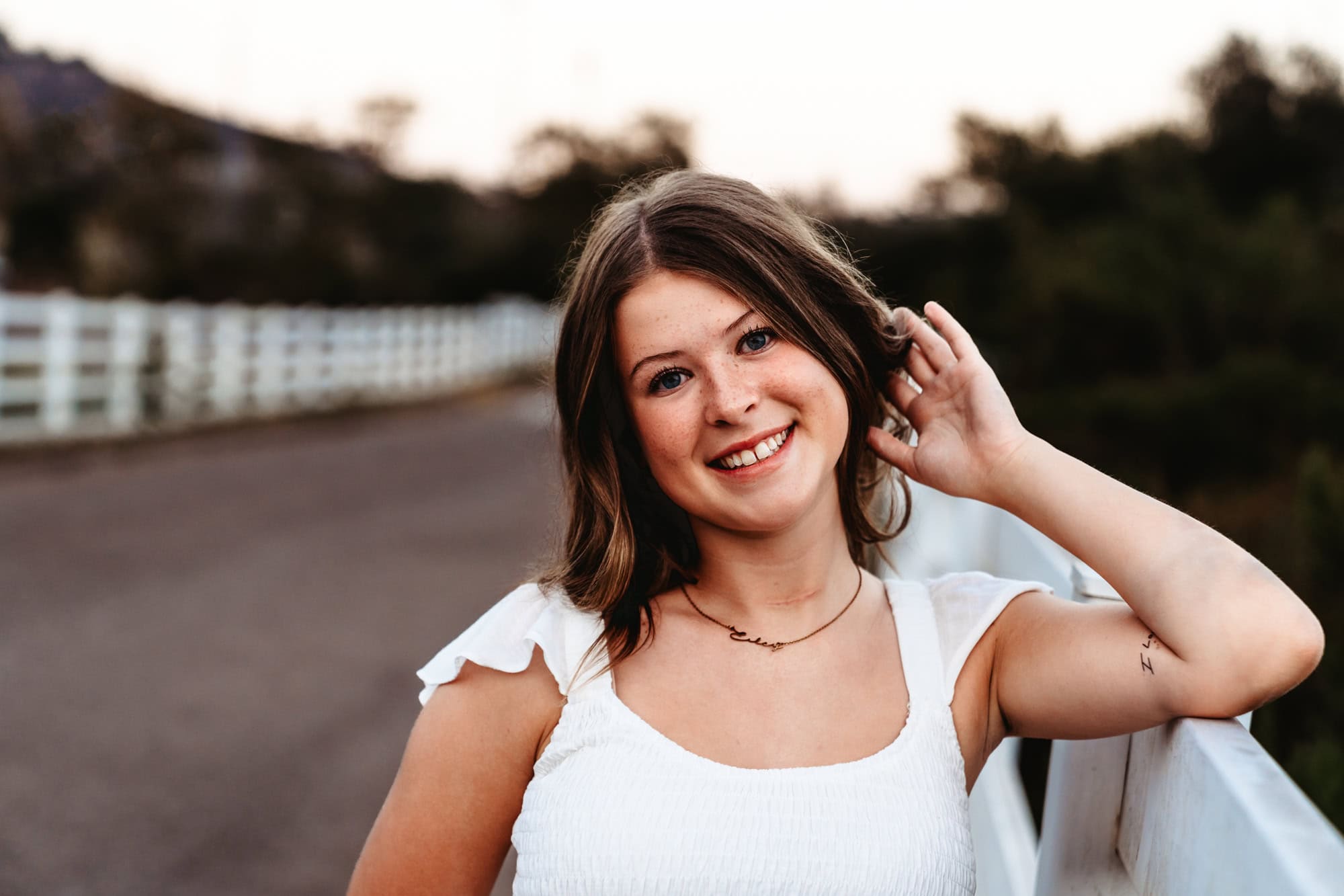 A senior girl leans against a white fence at Canyonside Park in San Diego during a fun outdoor senior photoshoot.