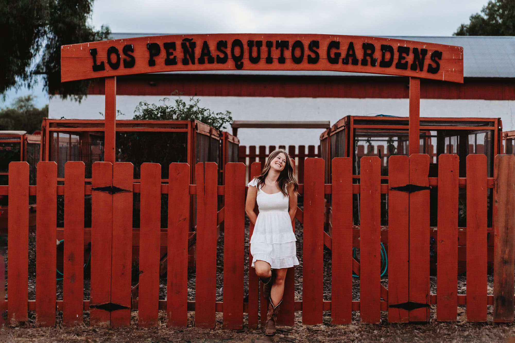 Senior portrait of girl in white dress at Los Peñasquitos Gardens sign, playful San Diego senior pictures.