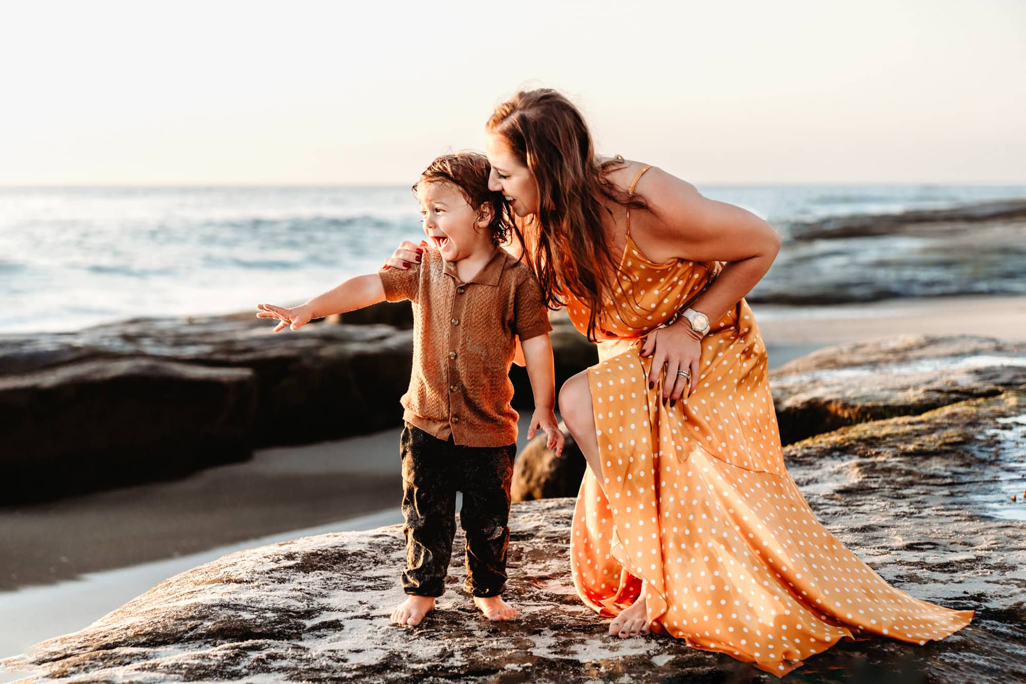 Mother kneeling beside her young son by the ocean on La Jolla's Windansea Beach.