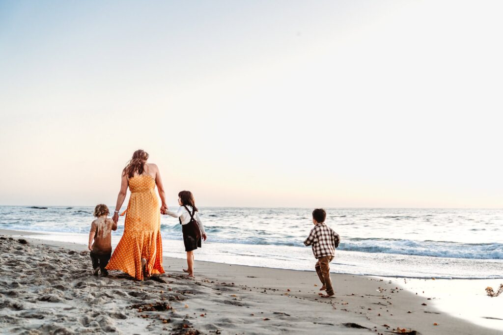 A mom walks along a La Jolla beach hand-in-hand with her children at sunset during a family photo session with Love Michelle Photography. 