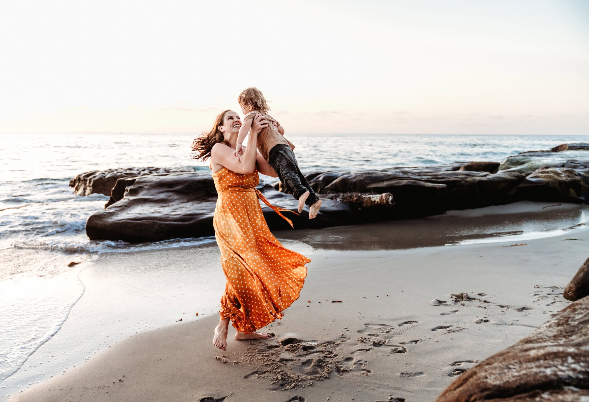 Mother twirling her child on a La Jolla beach in golden light during a San Diego family photoshoot with Love Michelle Photography.