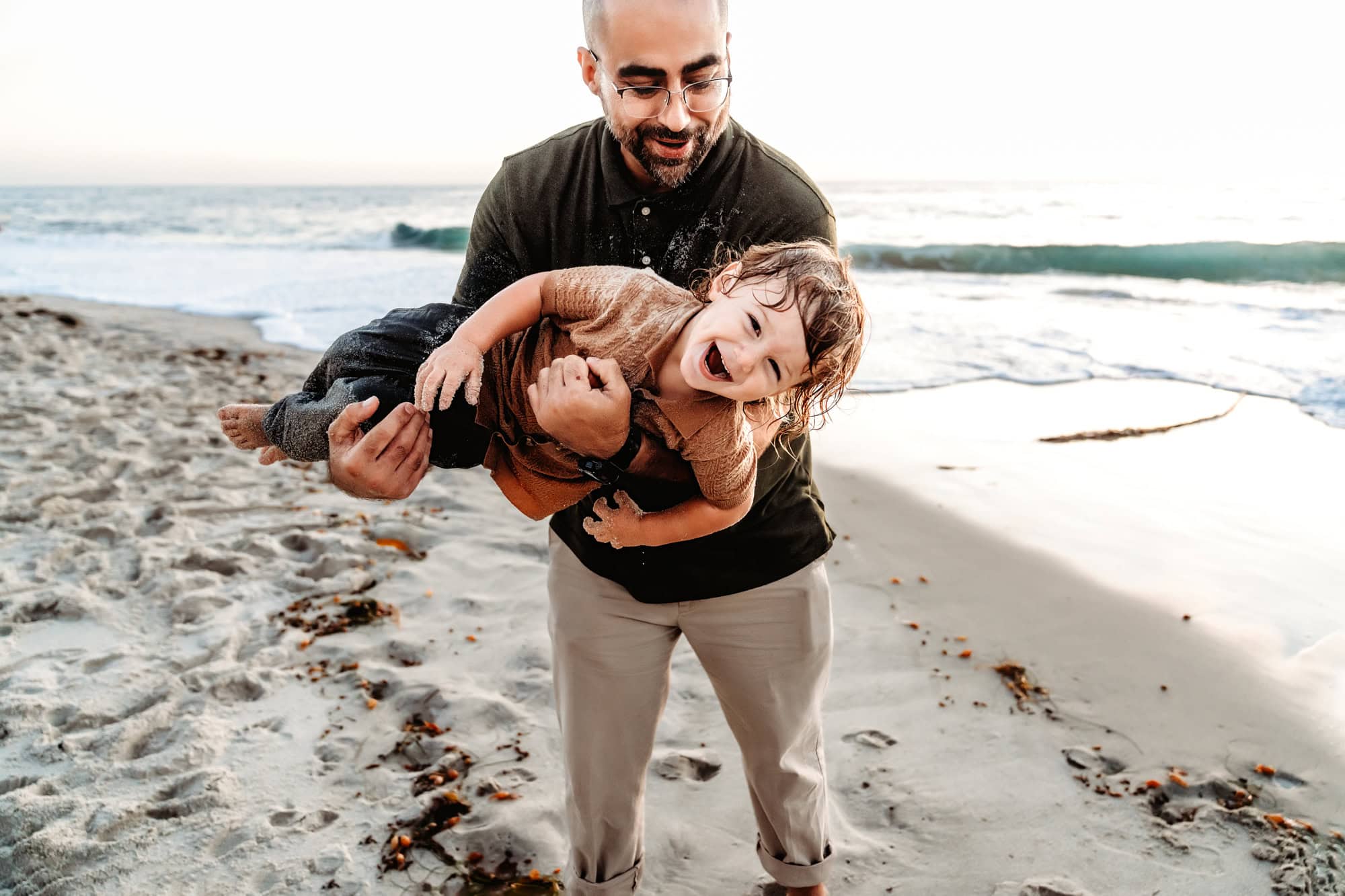 A father tosses his youngest child around during a fun family photoshoot at the Windansea beach.