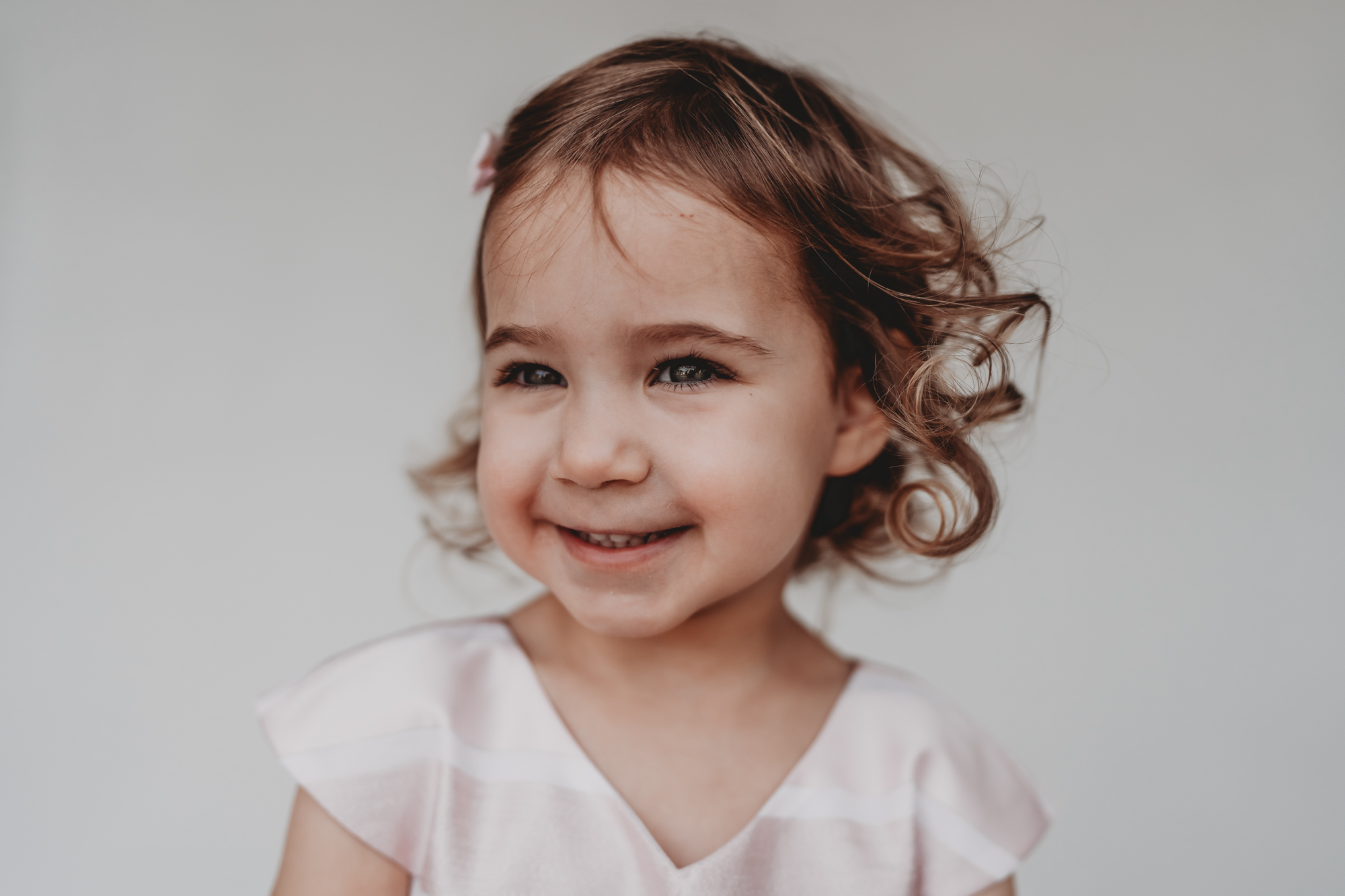 Fine art toddler school portrait of a curly-haired girl in a white dress, natural expression, San Diego. Love Michelle Photography