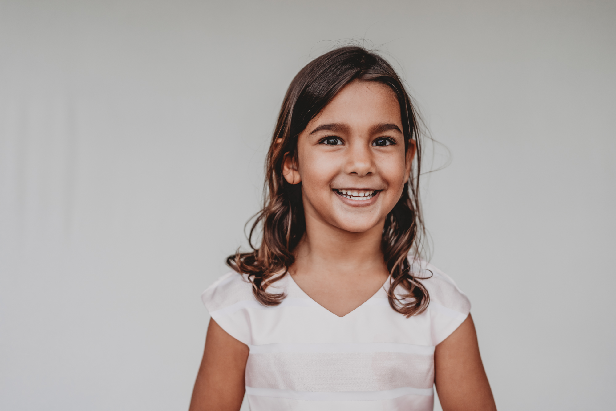 Fine art school photo of a smiling girl in a white top against a neutral backdrop, San Diego fine art school photograph