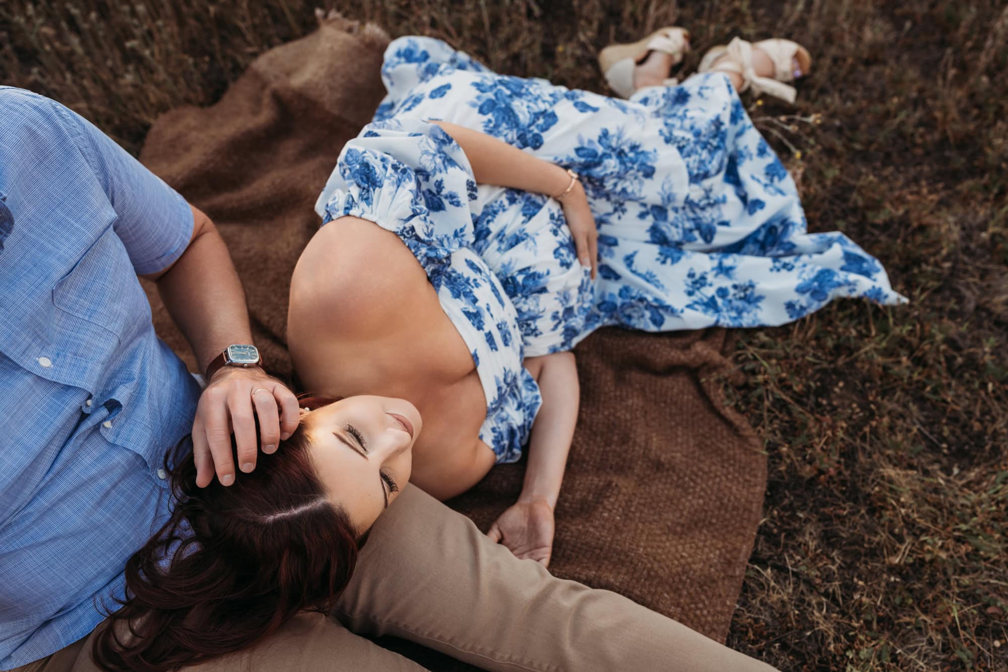 Artistic overhead maternity photo of pregnant couple lying together outdoors on blanket