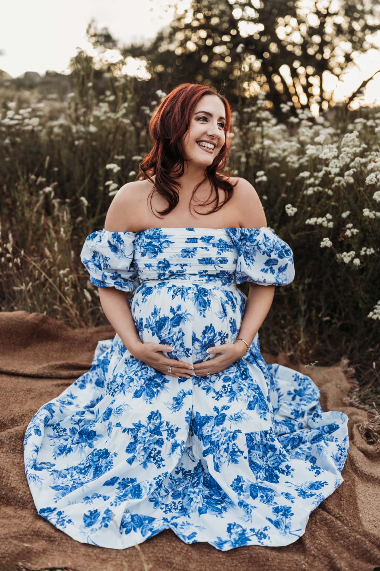 Pregnant mother in blue floral dress sitting outdoors during sunset maternity session in San Diego