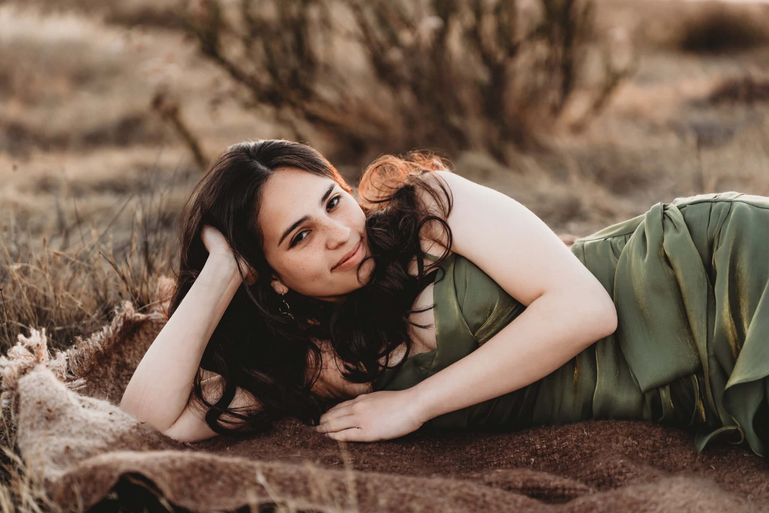 Senior girl in green dress reclining in a field, warm candid senior portrait by San Diego photographer