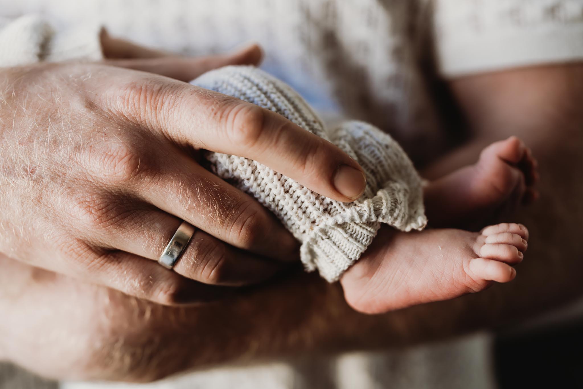 Close-up of a dad's hand gently holding his newborn baby's tiny feet during an in-home newborn photography session