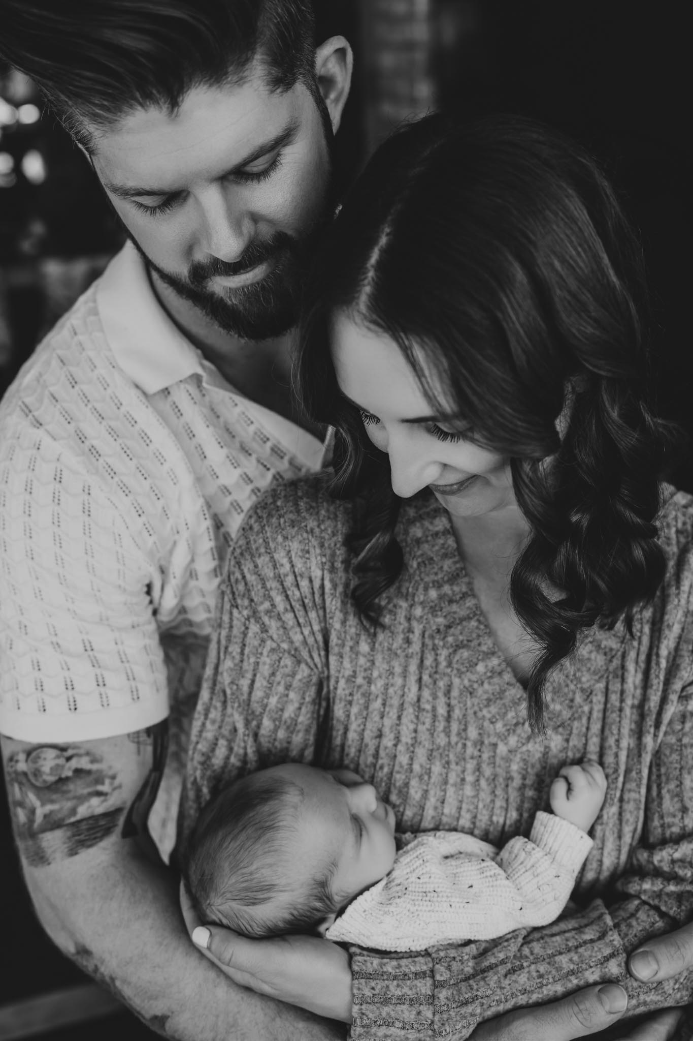 Black and white photo of new parents gazing lovingly at their sleeping newborn baby during an in-home newborn session in San Diego