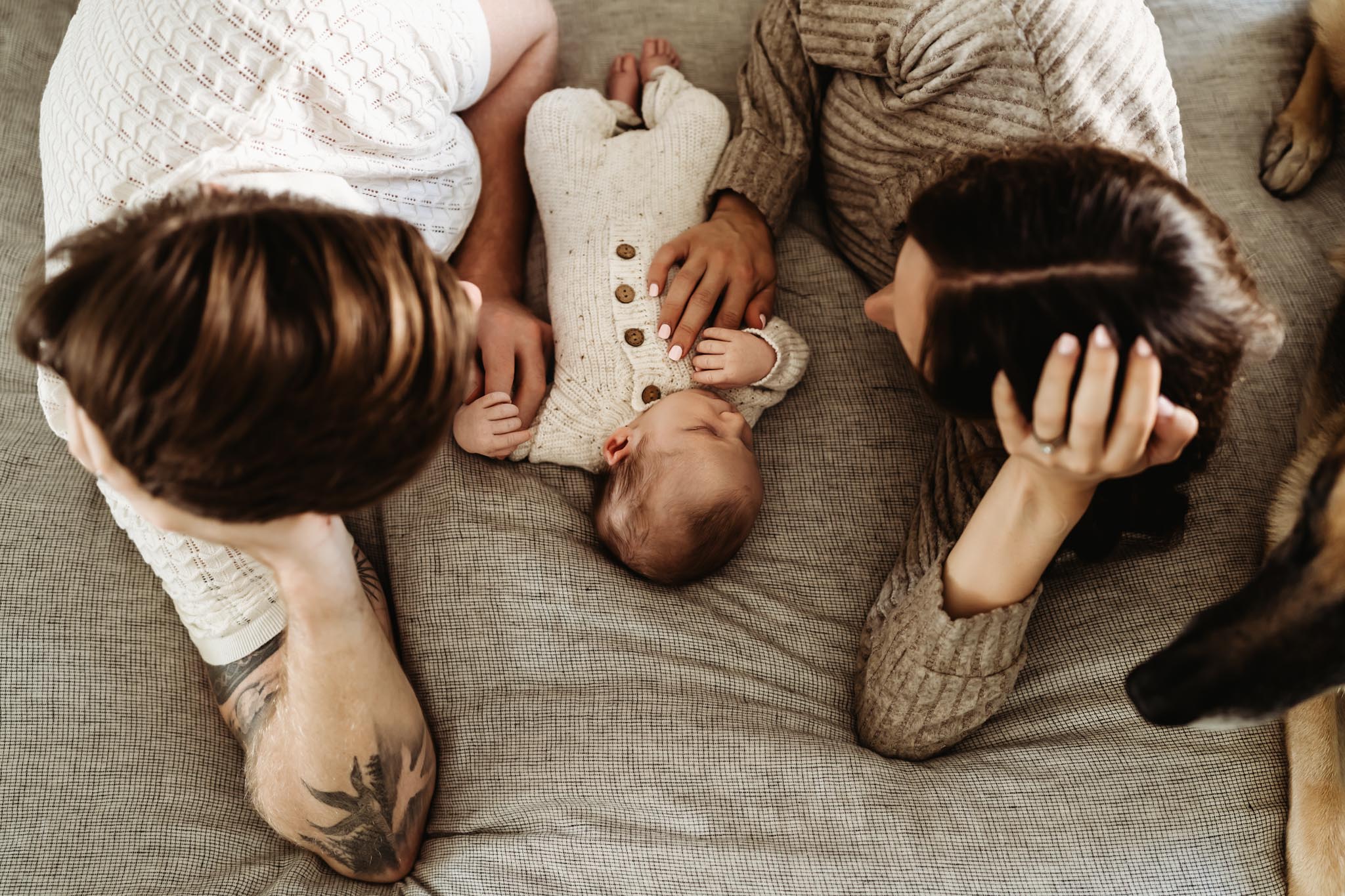 Overhead lifestyle newborn photo of mom, dad, newborn baby, and family dog relaxing together on a bed during an in-home newborn session in San Diego