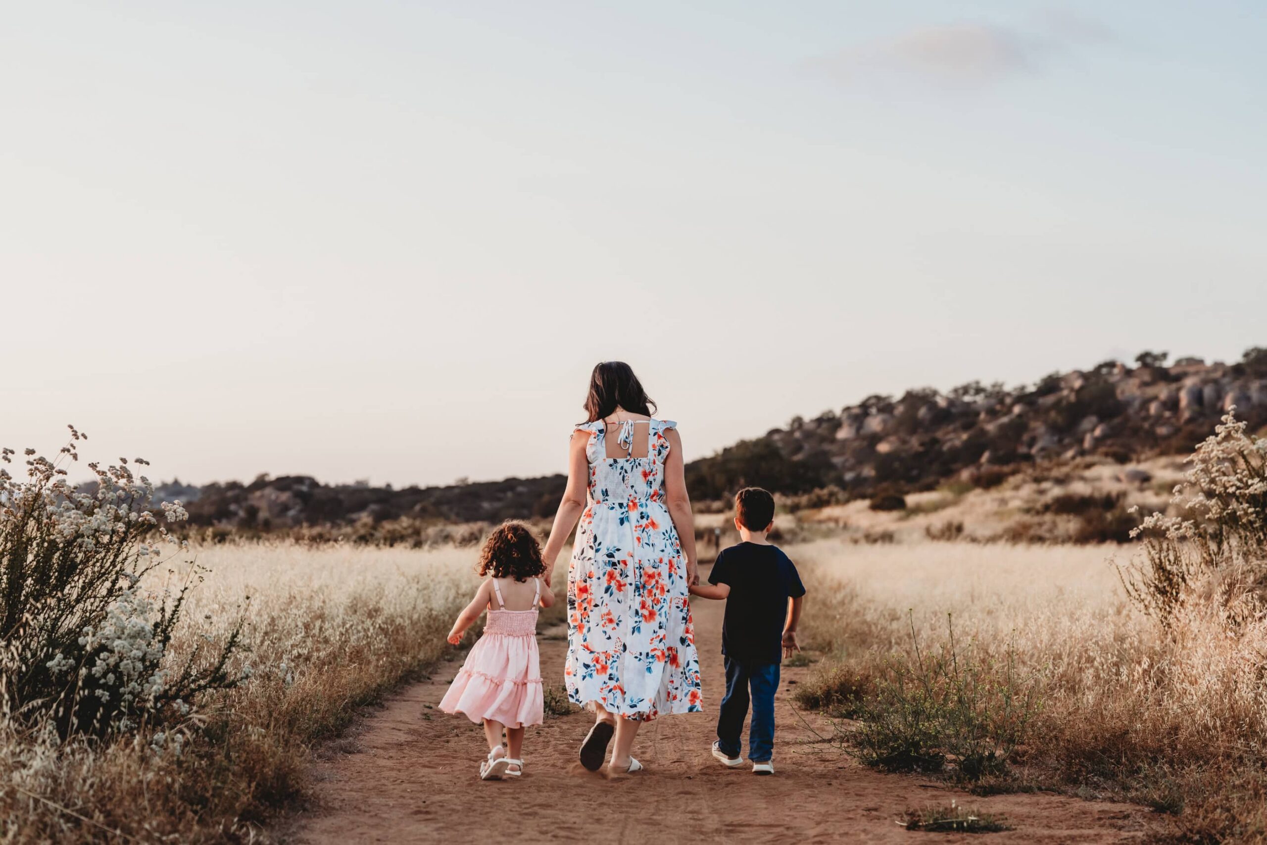 Mom walking down a sunlit path with her three children, a candid family moment captured by a San Diego family photographer